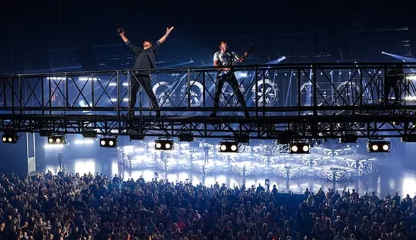 concert with a big crowd and two musicians standing on a rig above them playing guitar and singing